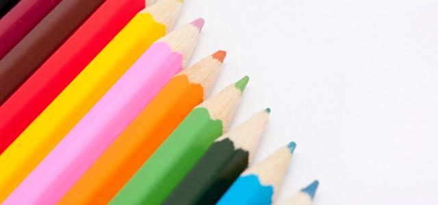 Row of coloured pencil crayons in the colours of the rainbow in a diagonal line with copyspace on a white background