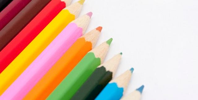 Row of coloured pencil crayons in the colours of the rainbow in a diagonal line with copyspace on a white background